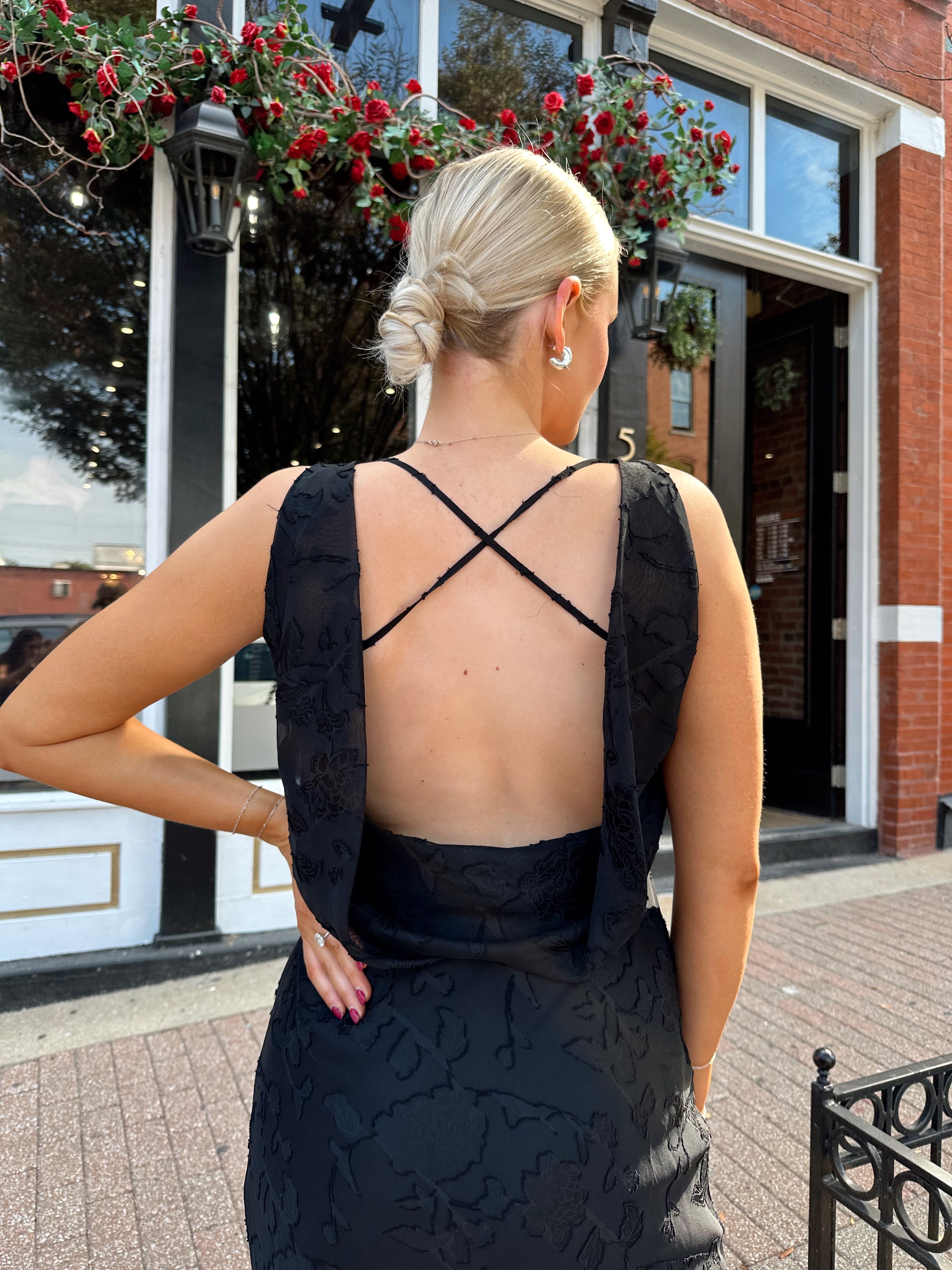 Woman wearing black textured midi dress with criss-cross cowl back. 