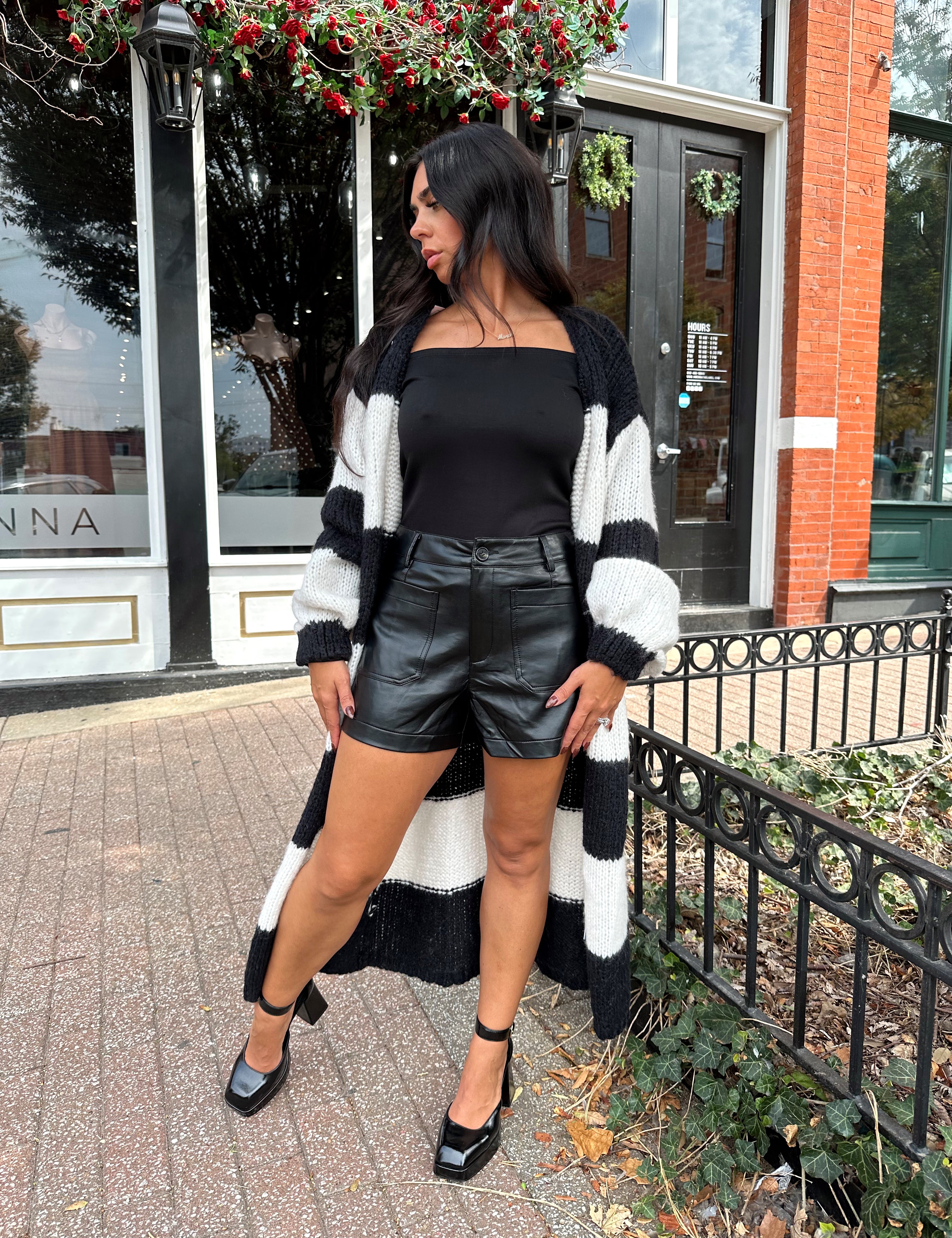 Woman wearing black and white striped knit long cardigan with black top and leather shorts.