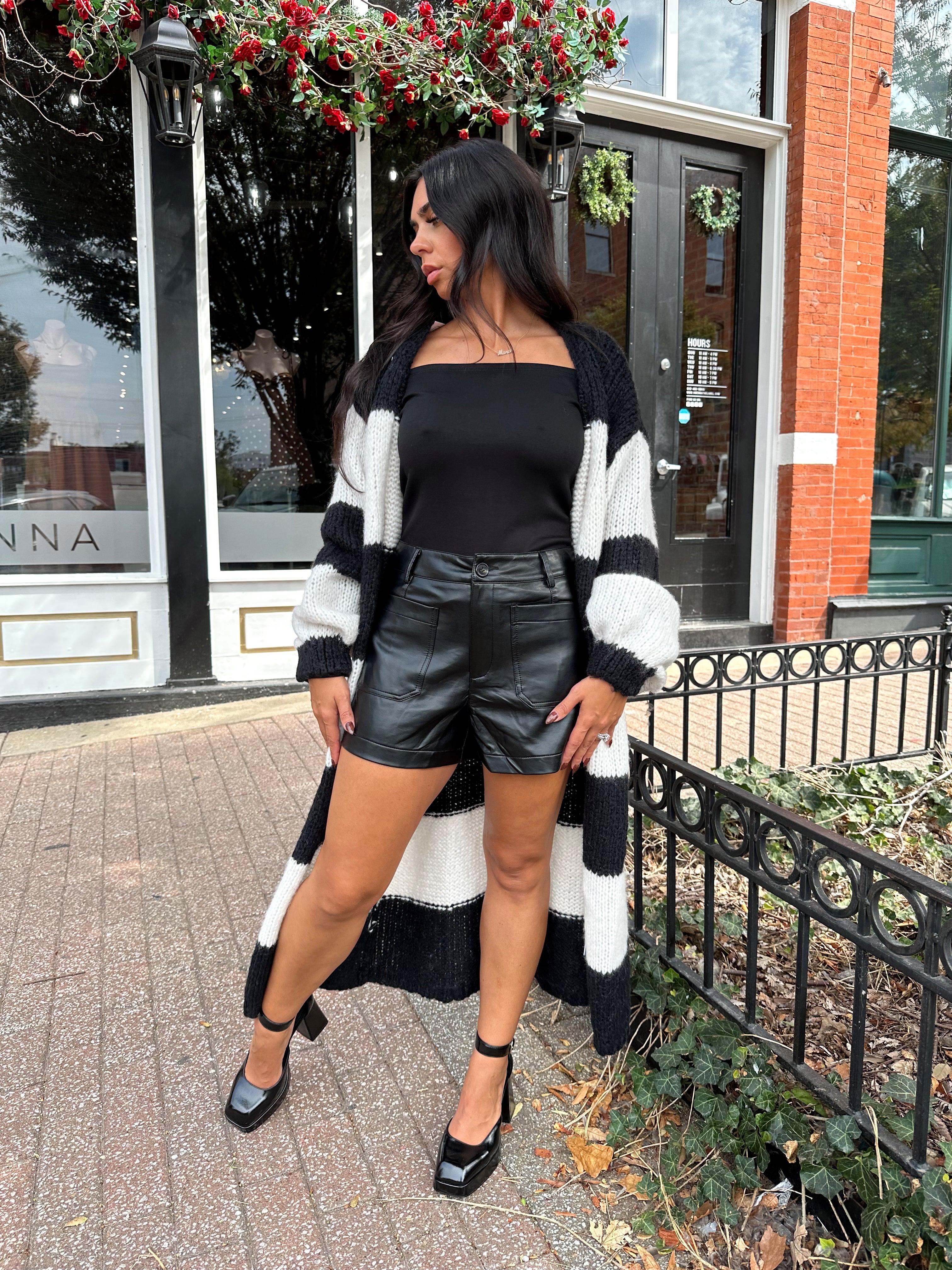 Woman wearing black and white striped knit long cardigan with black top and leather shorts.