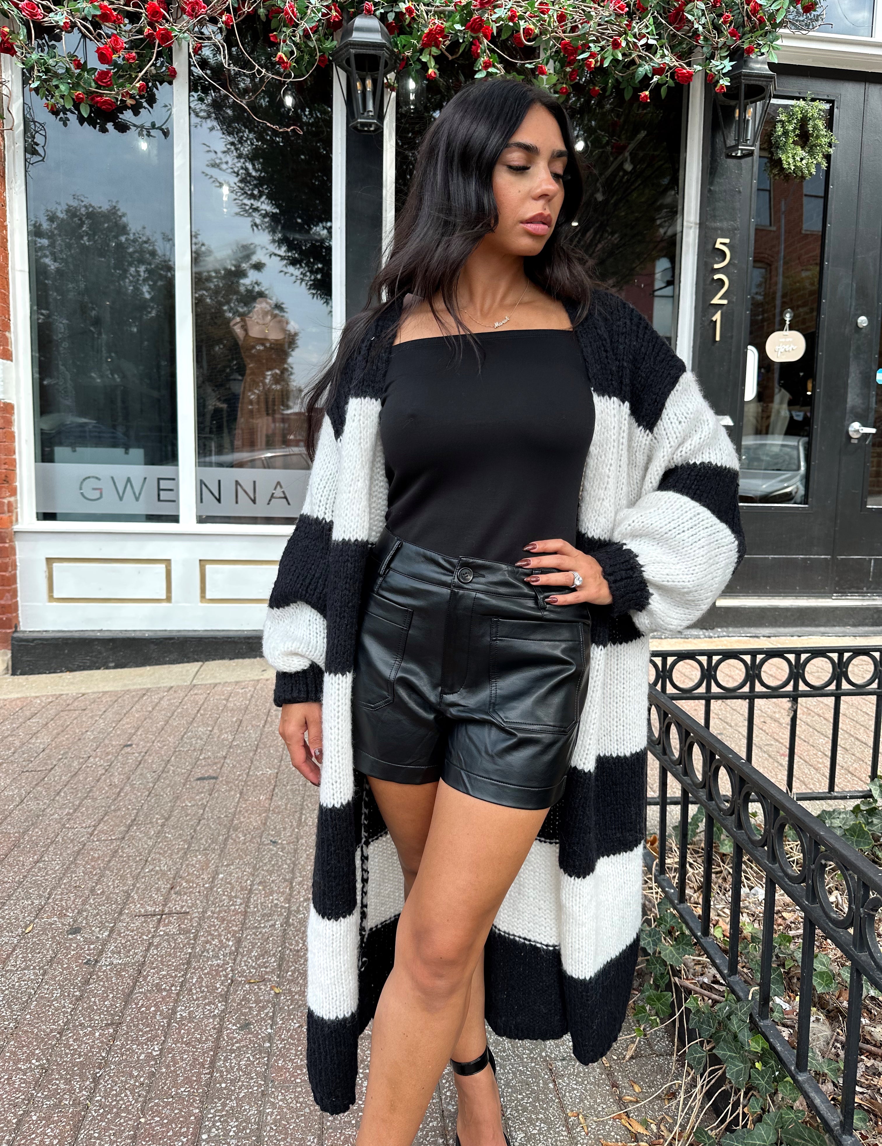 Woman wearing black and white striped knit long cardigan with black top and leather shorts.