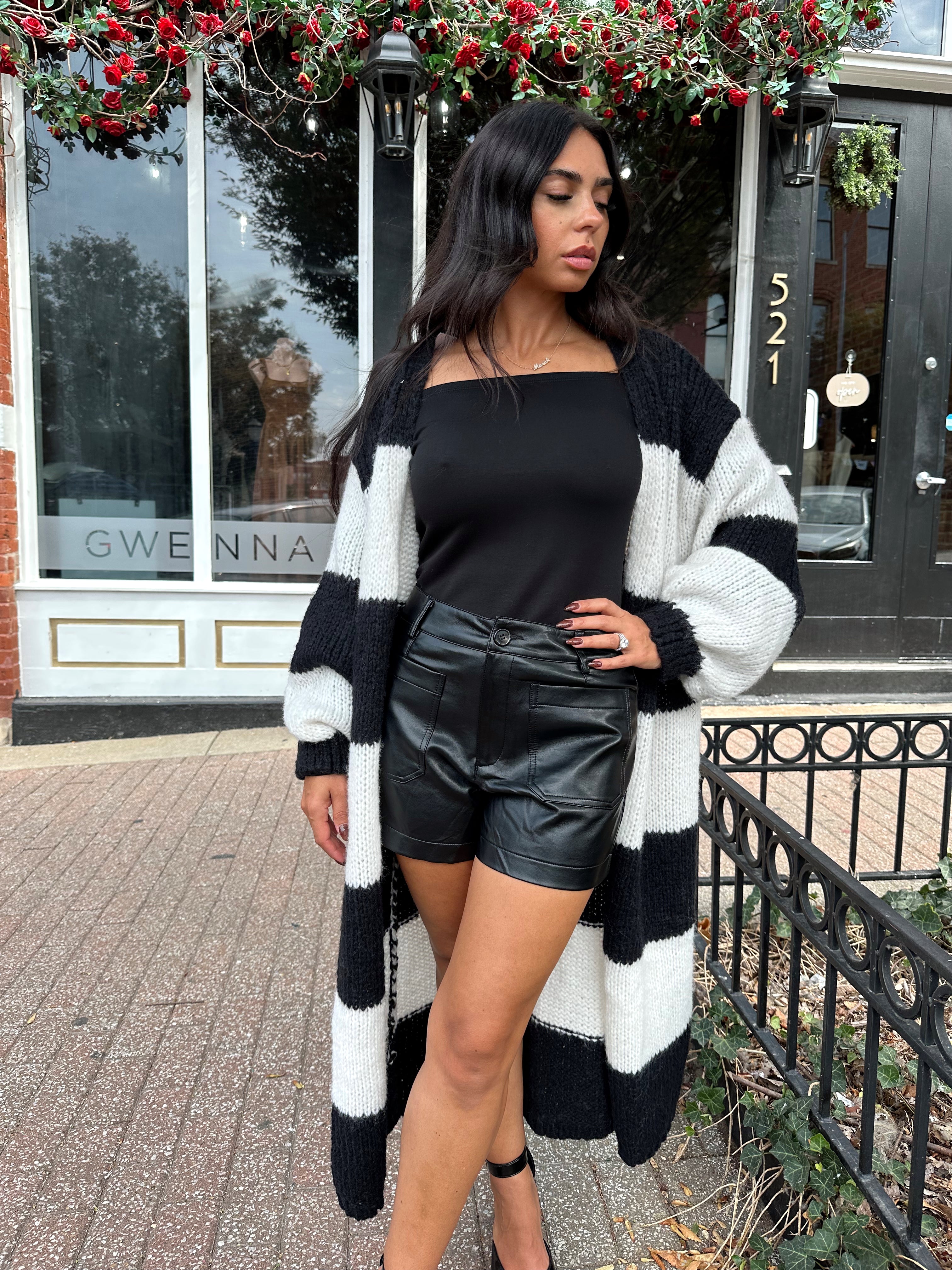 Woman wearing black and white striped knit long cardigan with black top and leather shorts.