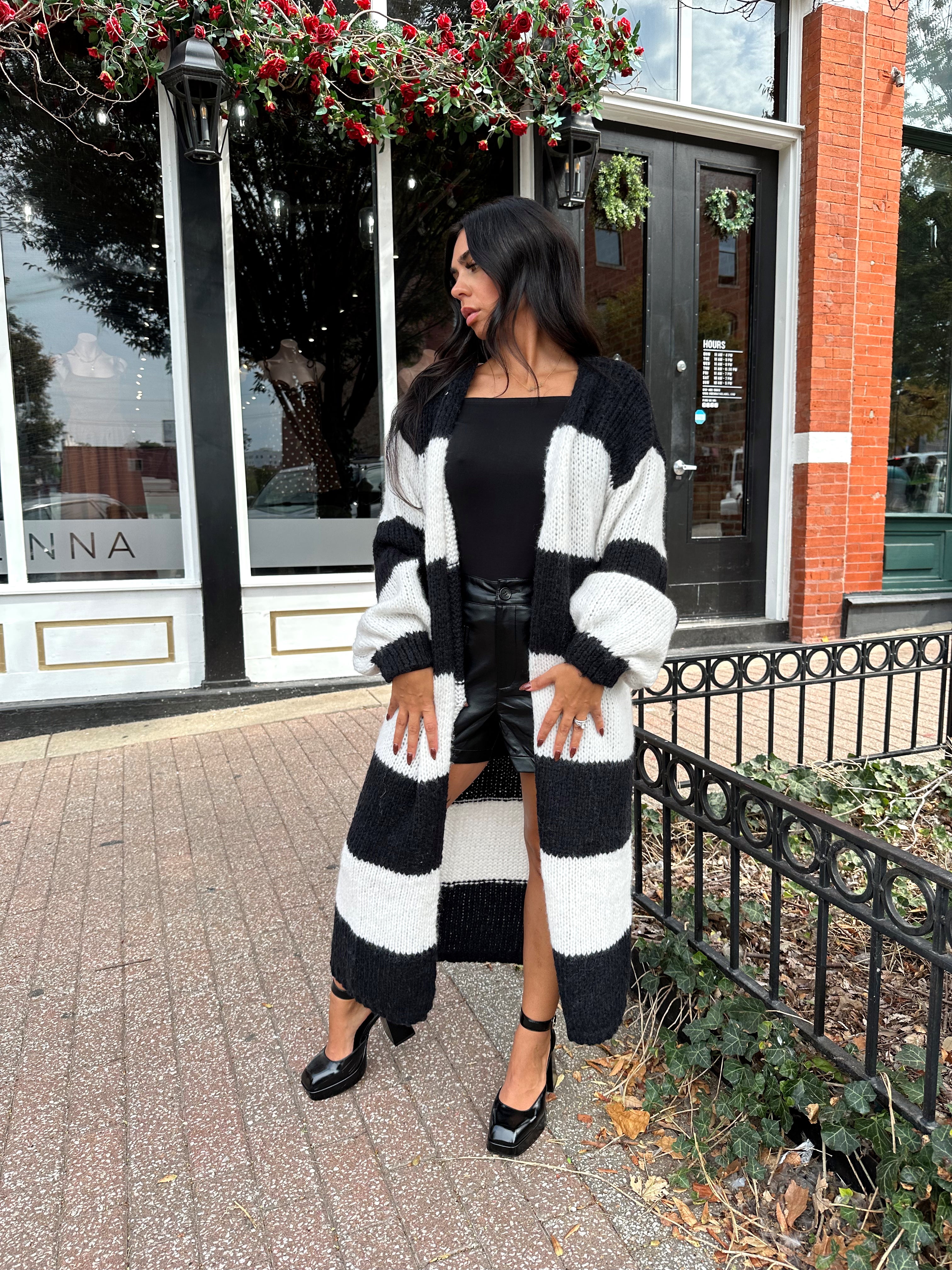 Woman wearing black and white striped knit long cardigan with black top and leather shorts.