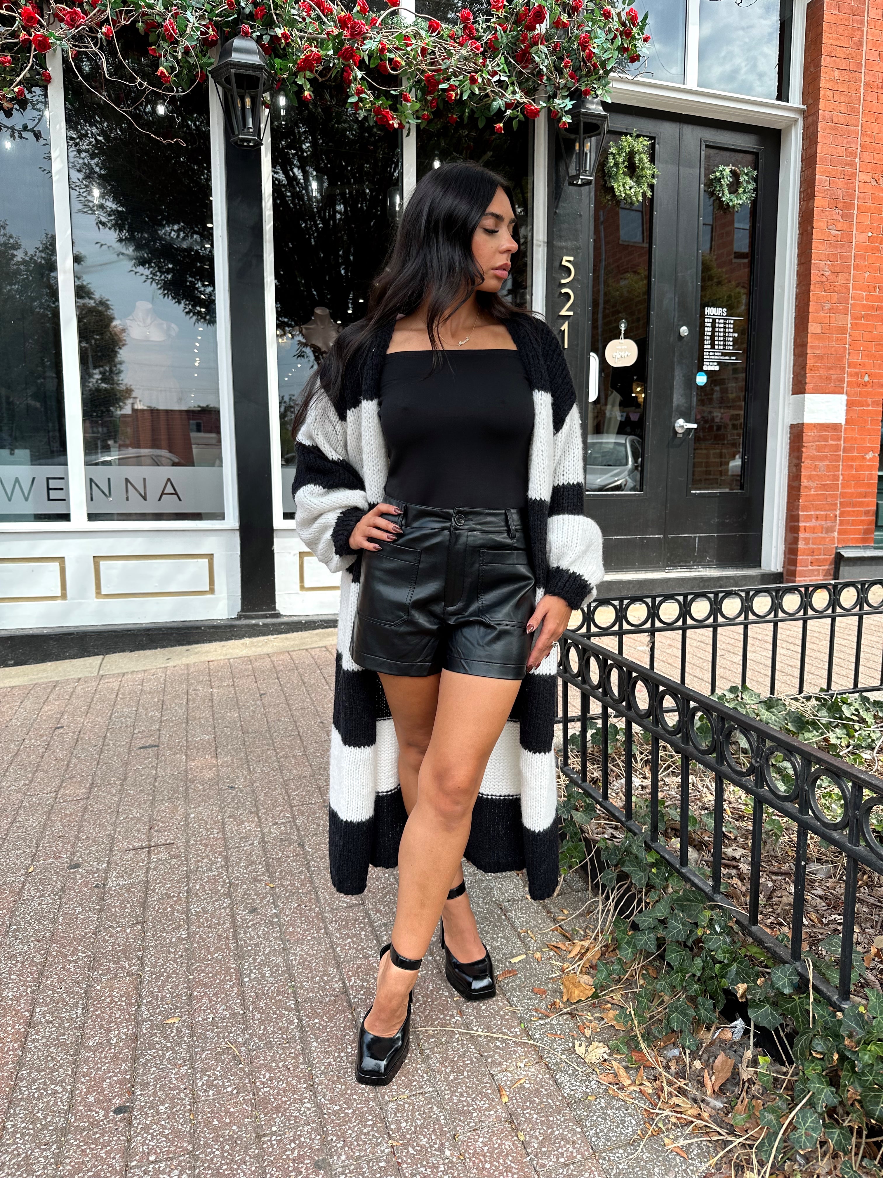 Woman wearing black and white striped knit long cardigan with black top and leather shorts.