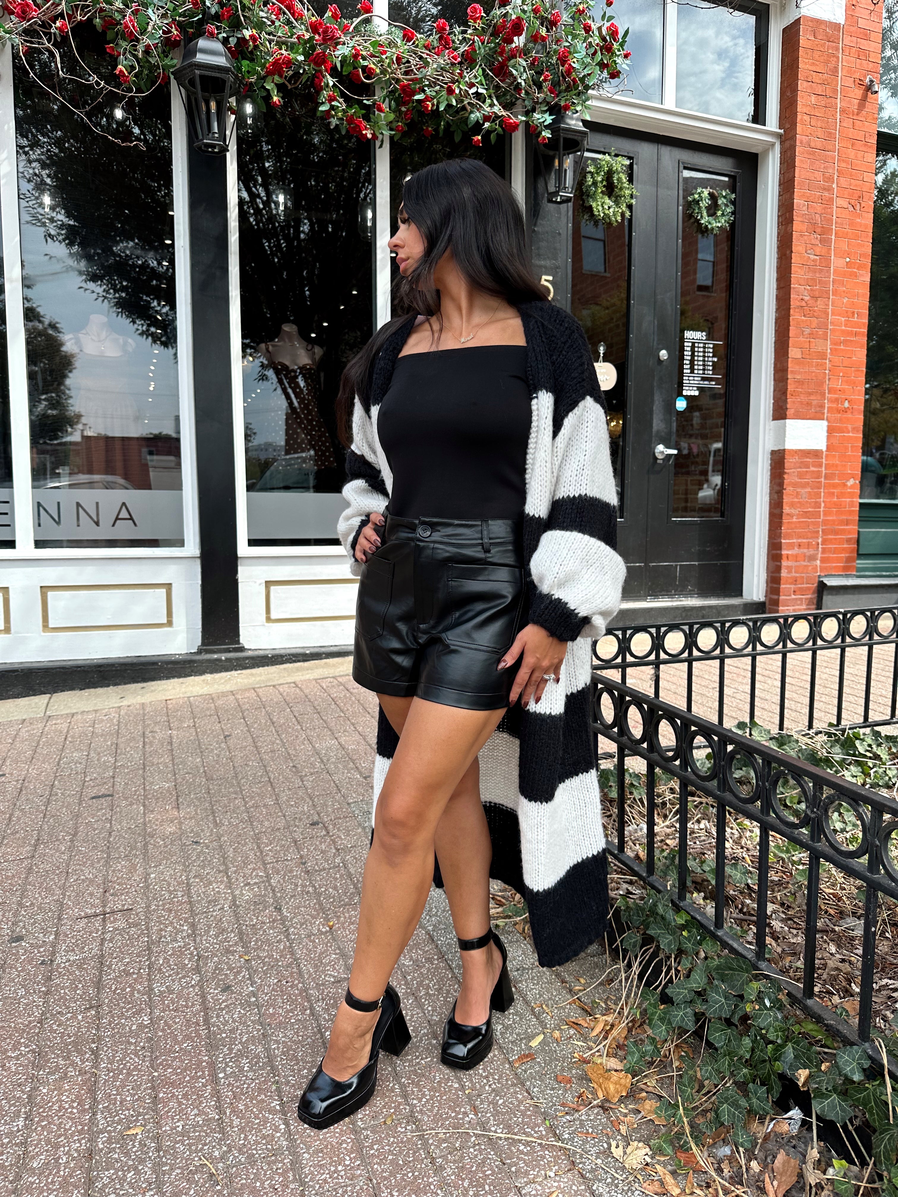 Woman wearing black and white striped knit long cardigan with black top and leather shorts.