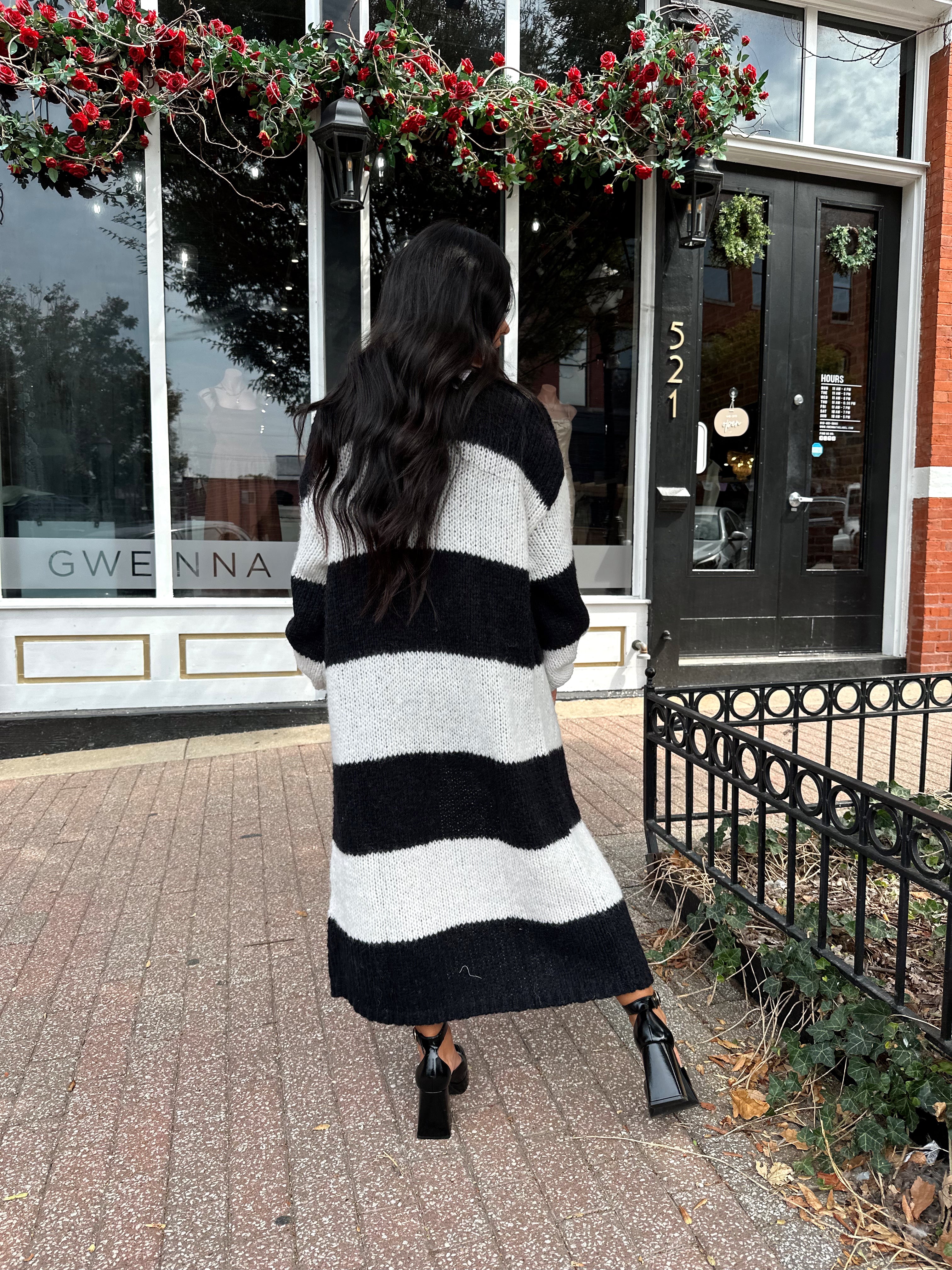 Woman wearing black and white striped knit long cardigan with black top and leather shorts.