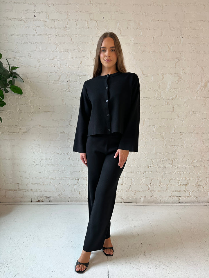 Woman wearing black knit two piece lounge set with long sleeve button down sweater and wide leg pant. 
