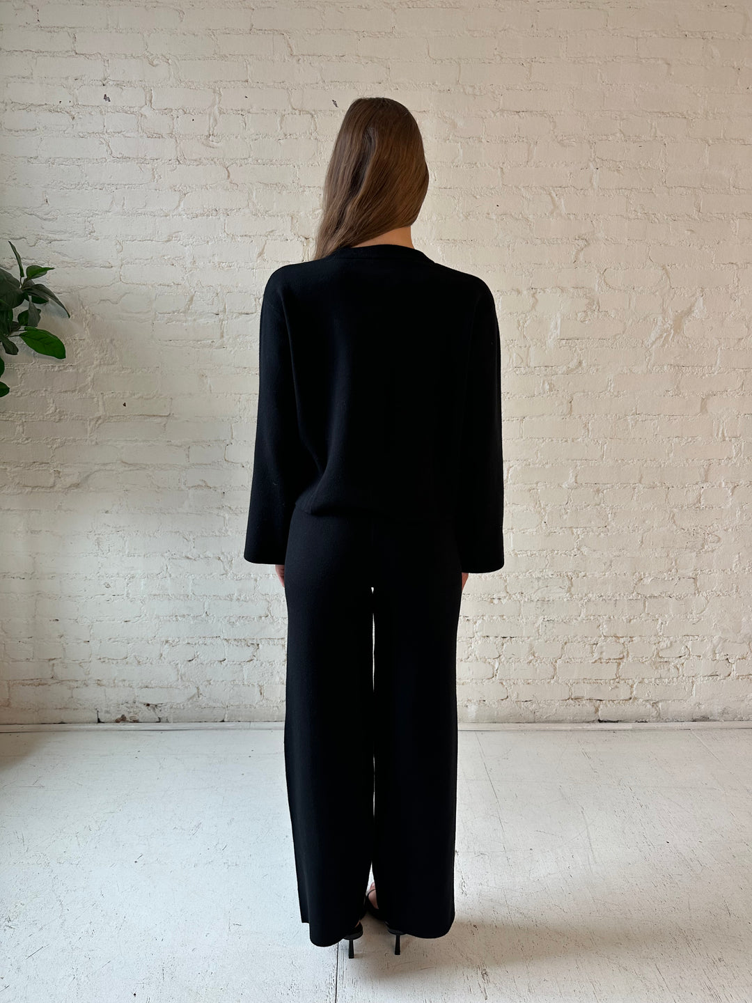 Woman wearing black knit two piece lounge set with long sleeve button down sweater and wide leg pant. 
