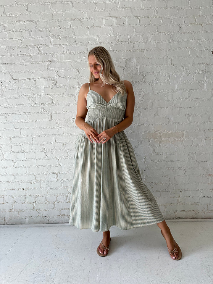 Woman wearing sage green striped midi dress with functional pockets.