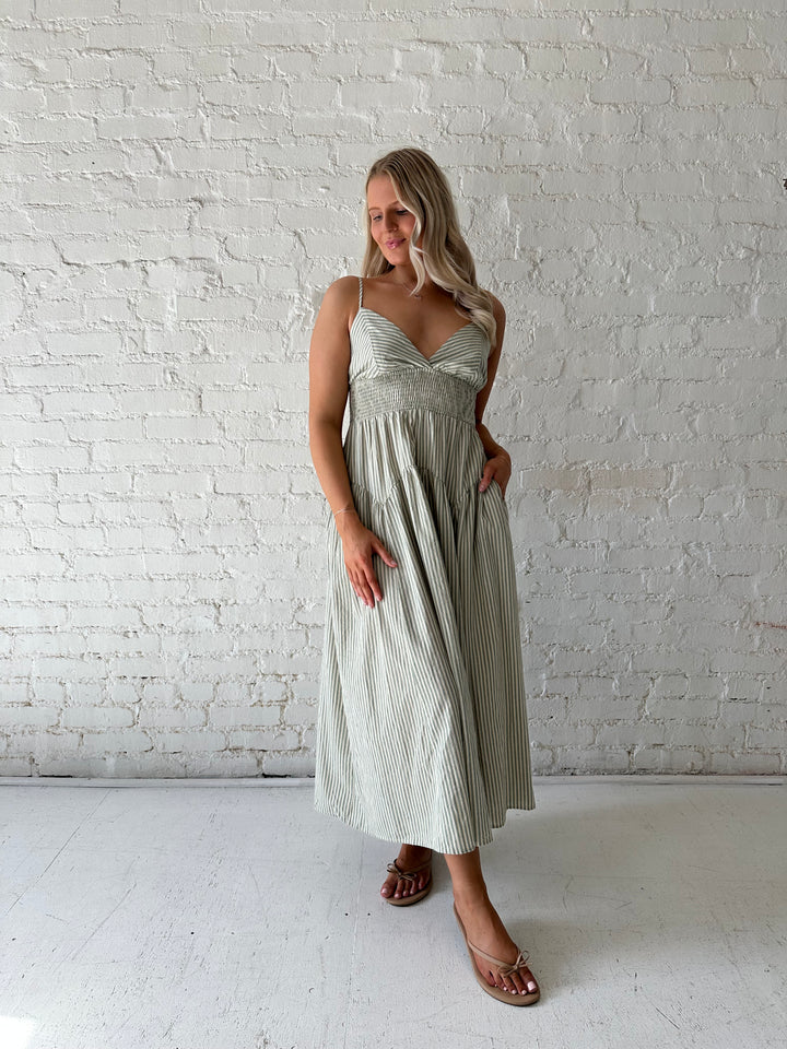 Woman wearing sage green striped midi dress with functional pockets.