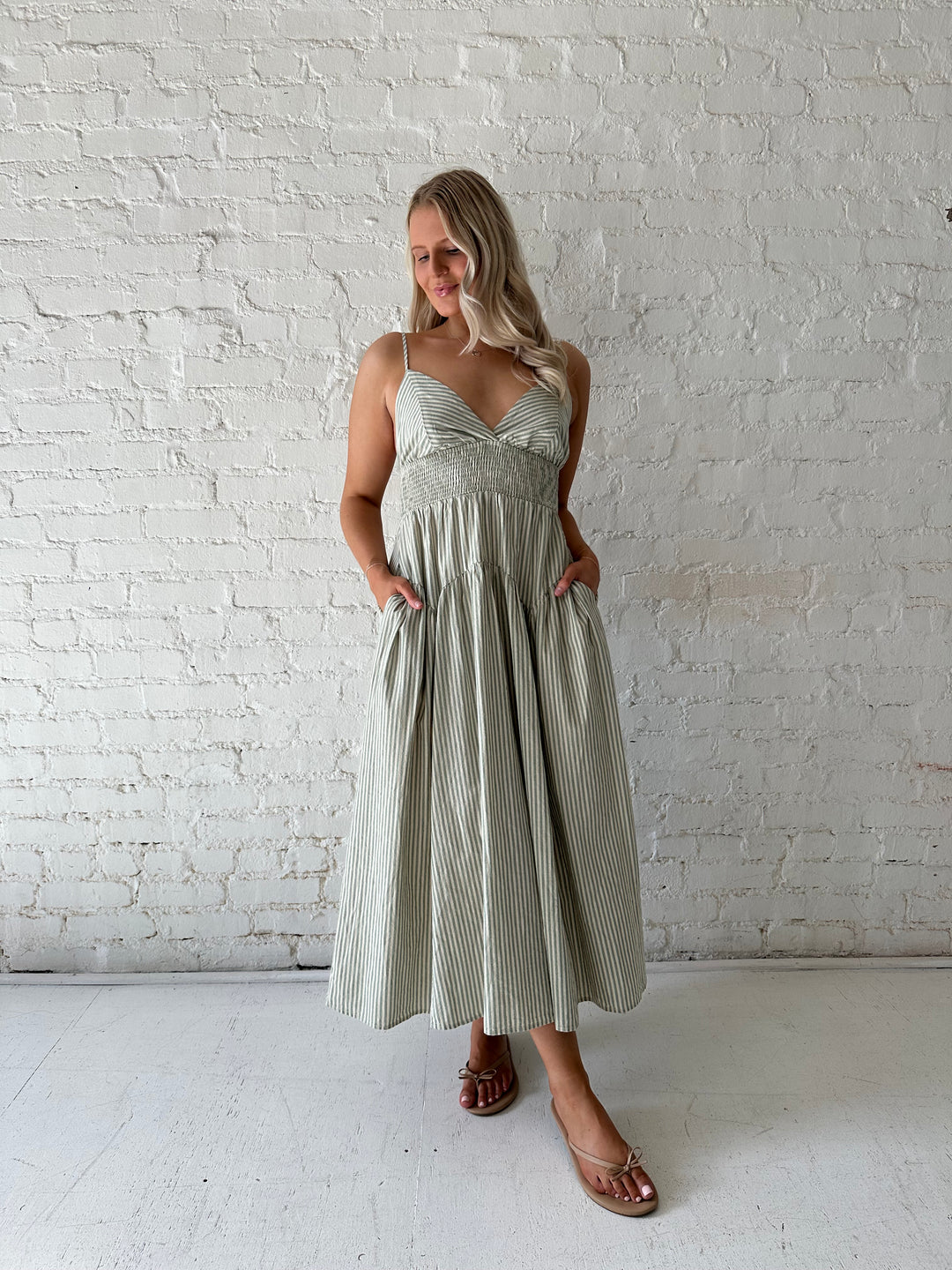 Woman wearing sage green striped midi dress with functional pockets.