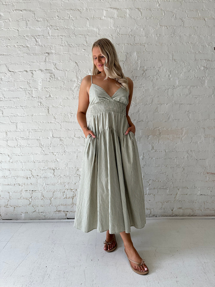 Woman wearing sage green striped midi dress with functional pockets.