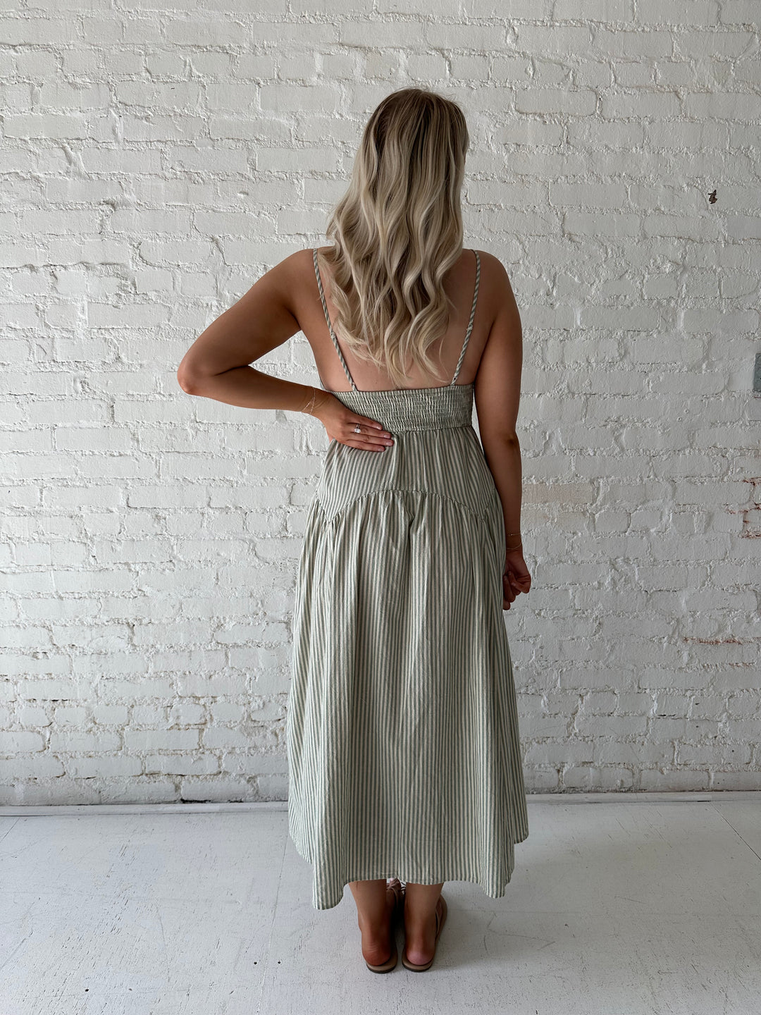 Woman wearing sage green striped midi dress with functional pockets.