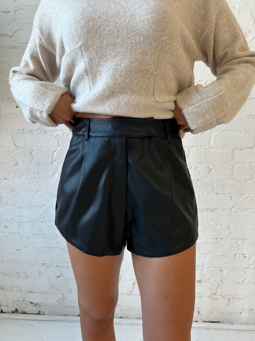Woman wearing black faux leather high waisted pleated shorts and knit sweater. 