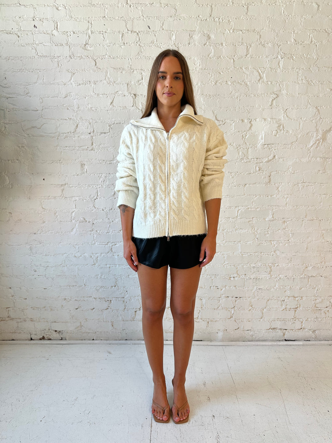 Woman wearing black faux leather high waisted pleated shorts and knit sweater. 