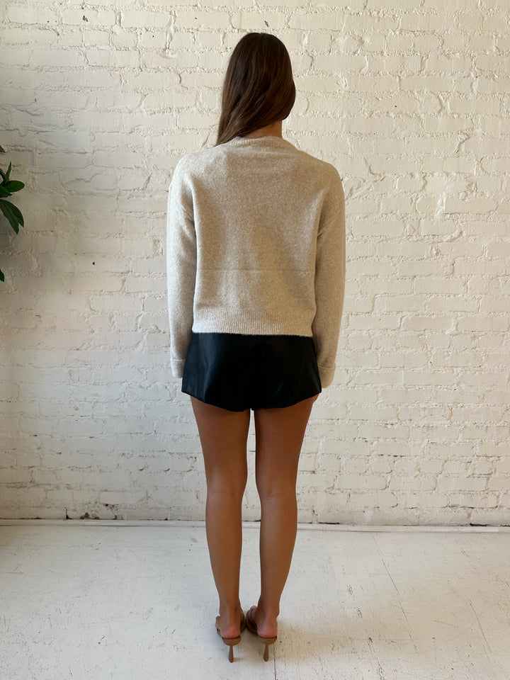 Woman wearing black faux leather high waisted pleated shorts and knit sweater. 
