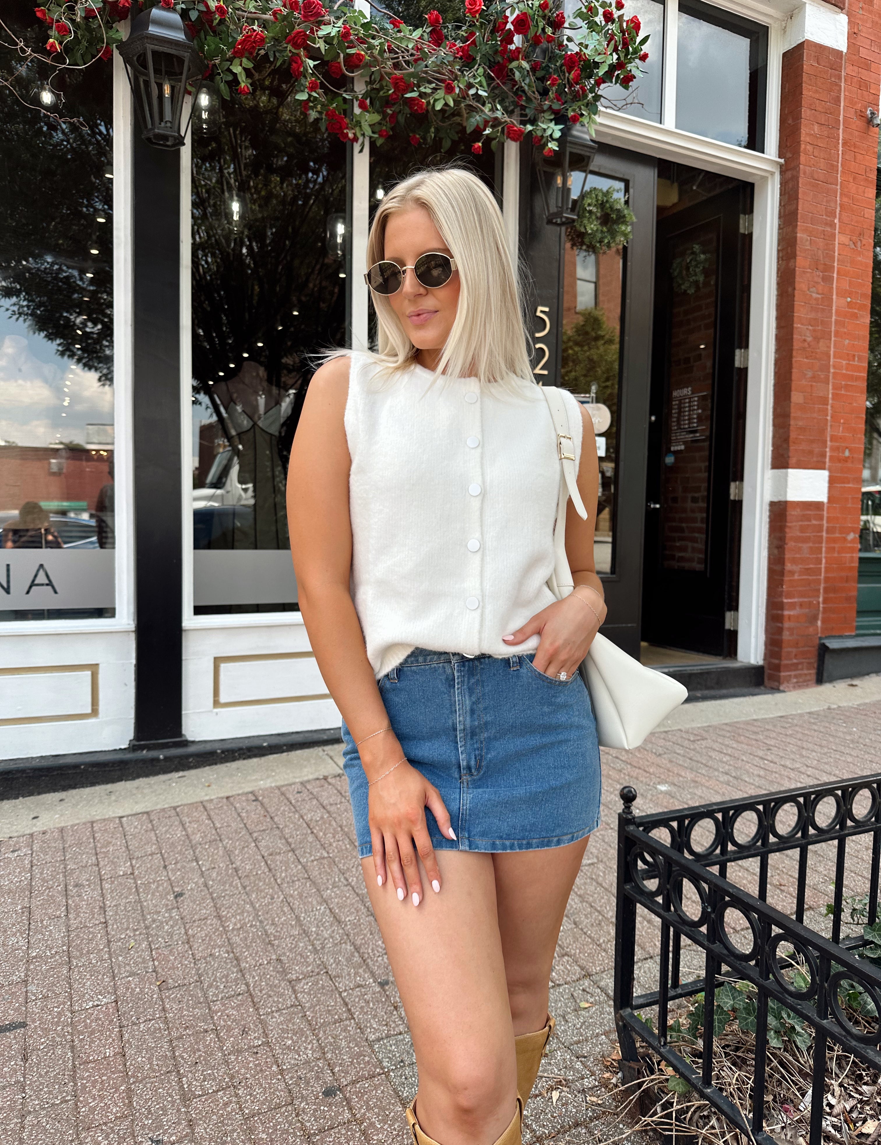 Woman wearing a white knit sleeveless sweater top with a denim mini skirt.