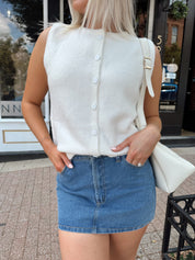 Woman wearing a white knit sleeveless sweater top with a denim mini skirt.