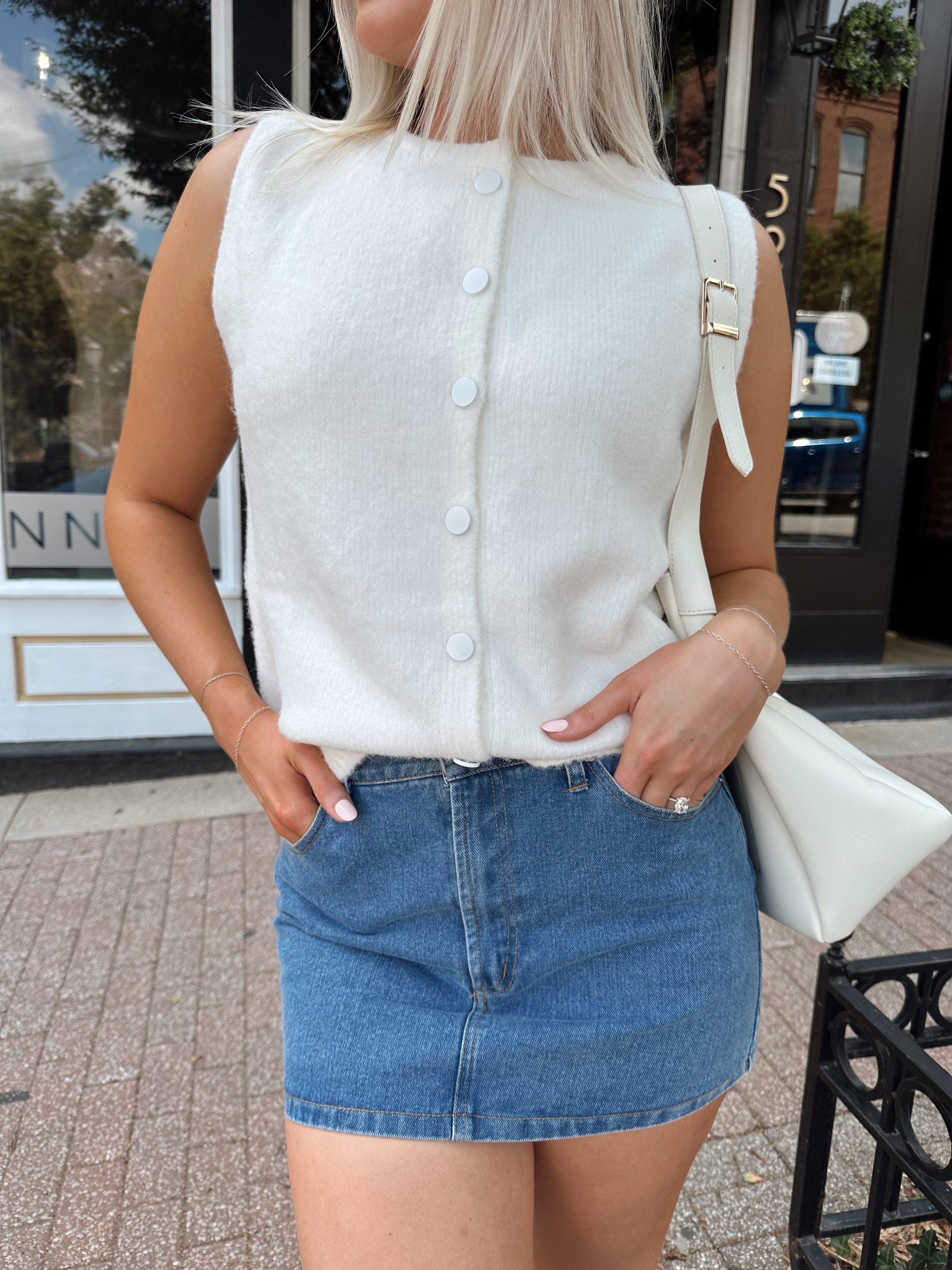 Woman wearing a white knit sleeveless sweater top with a denim mini skirt.