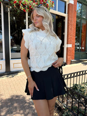 Woman wearing cream cable knit sleeveless sweater with black bow side detail. 