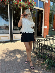 Woman wearing cream cable knit sleeveless sweater with black bow side detail. 