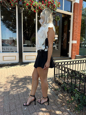 Woman wearing cream cable knit sleeveless sweater with black bow side detail. 