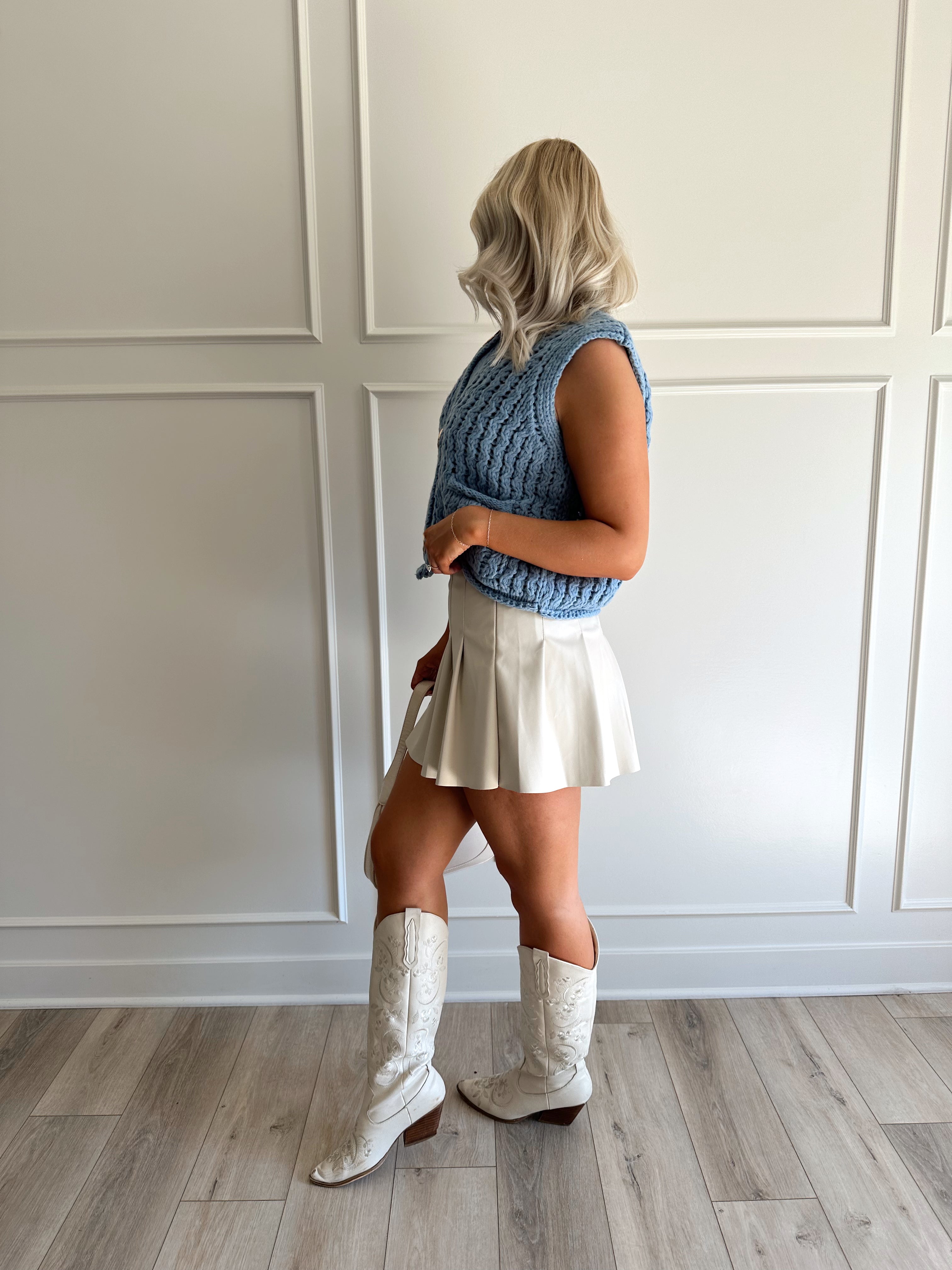 Woman wearing a light blues chunky sleeveless sweater with gold button closure.