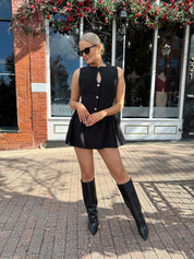 Woman wearing fit to flare black mini dress with keyhole cutout and gold buttons.