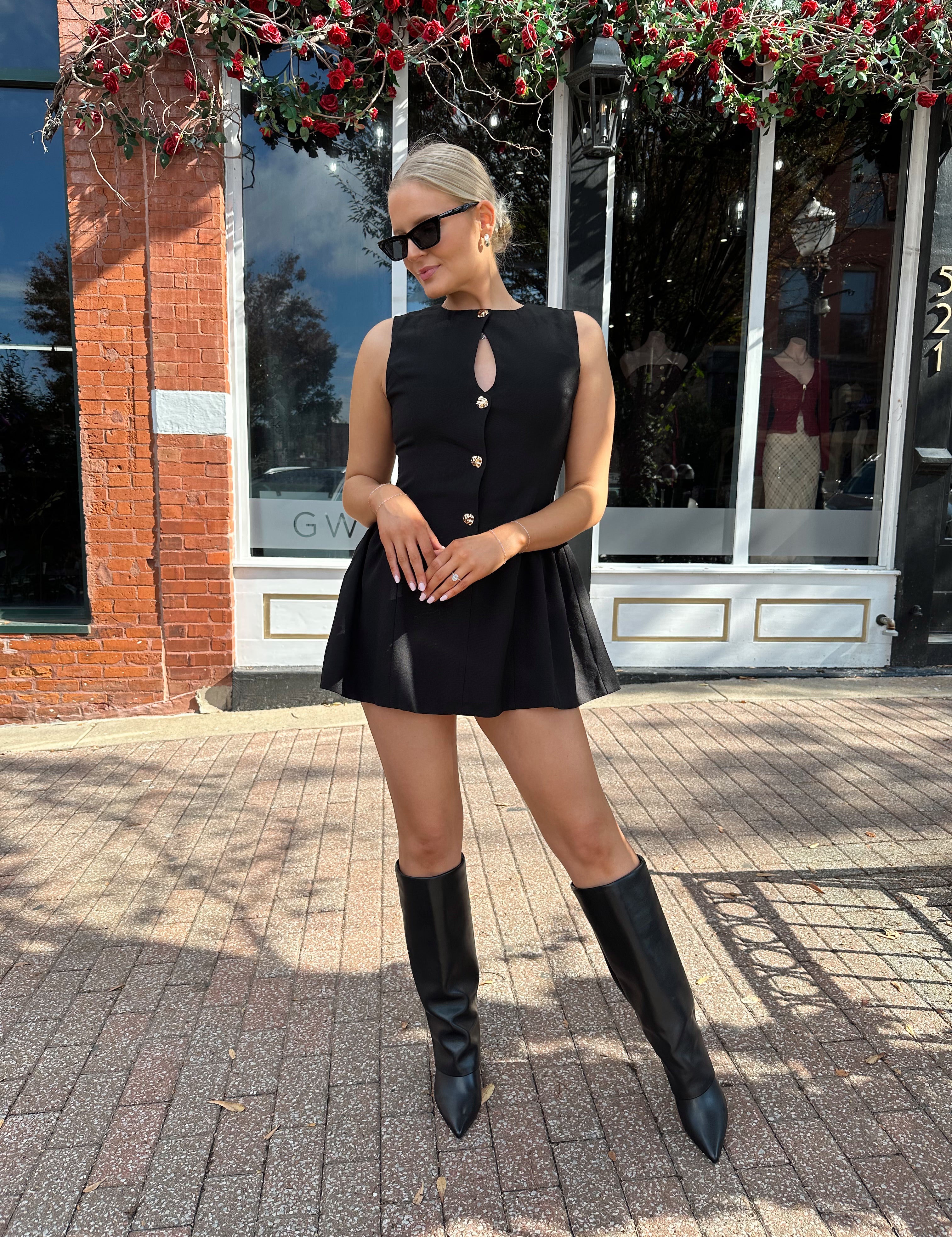 Woman wearing fit to flare black mini dress with keyhole cutout and gold buttons.