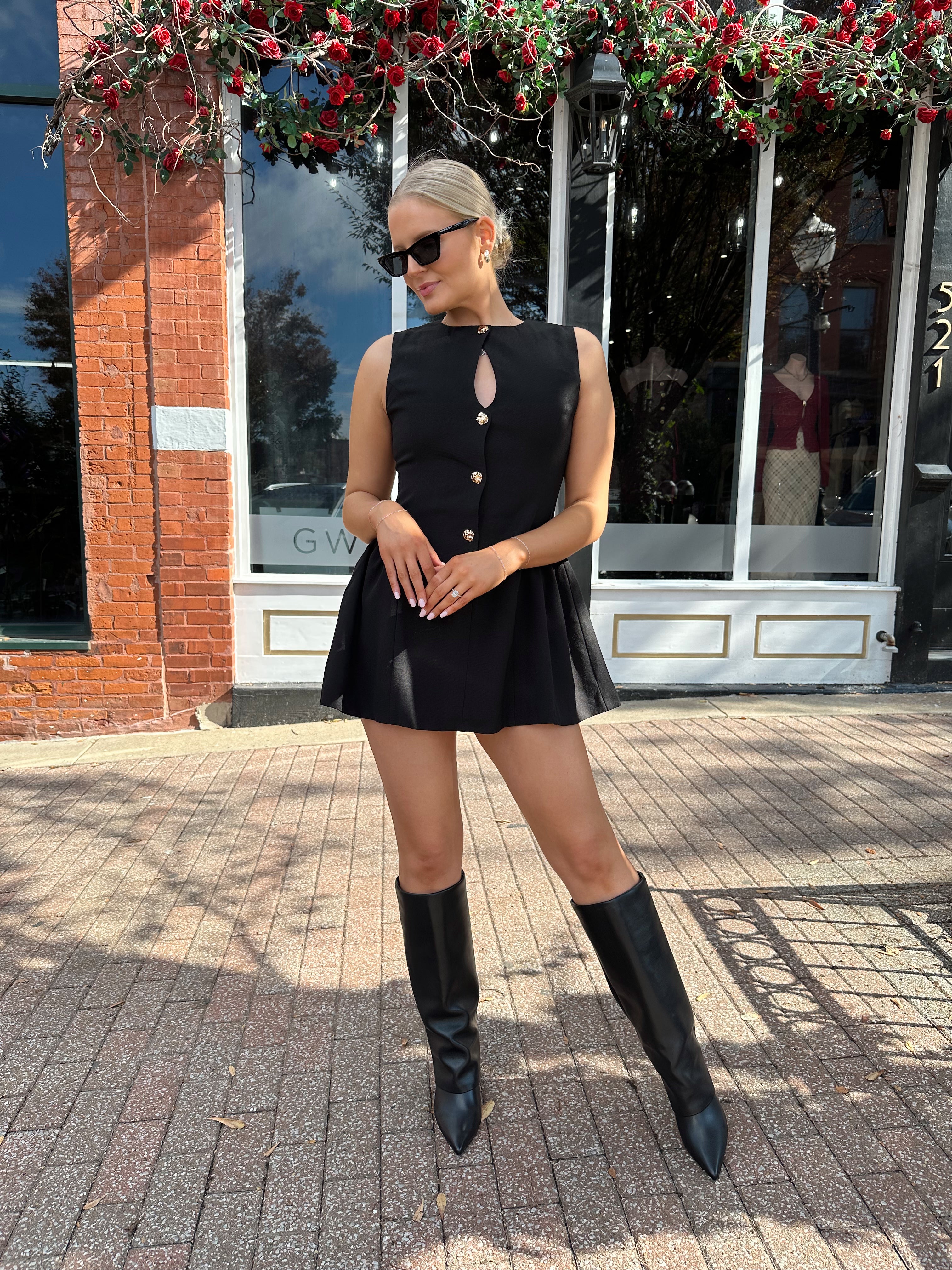 Woman wearing fit to flare black mini dress with keyhole cutout and gold buttons.