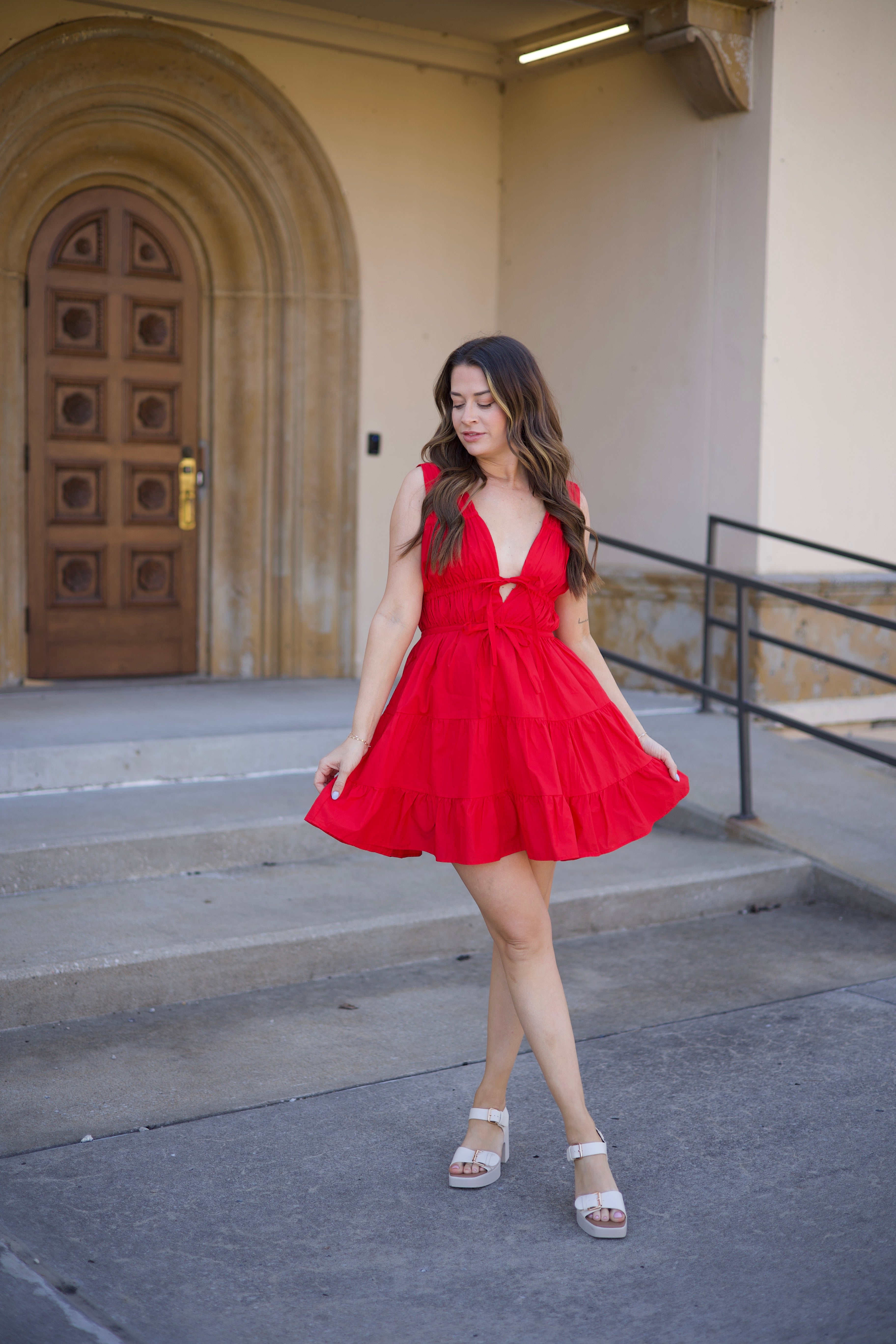 Kerry Tiered Mini Dress in red with a plunging neckline and tiered ruffles, twirling in front of an arched doorway.
