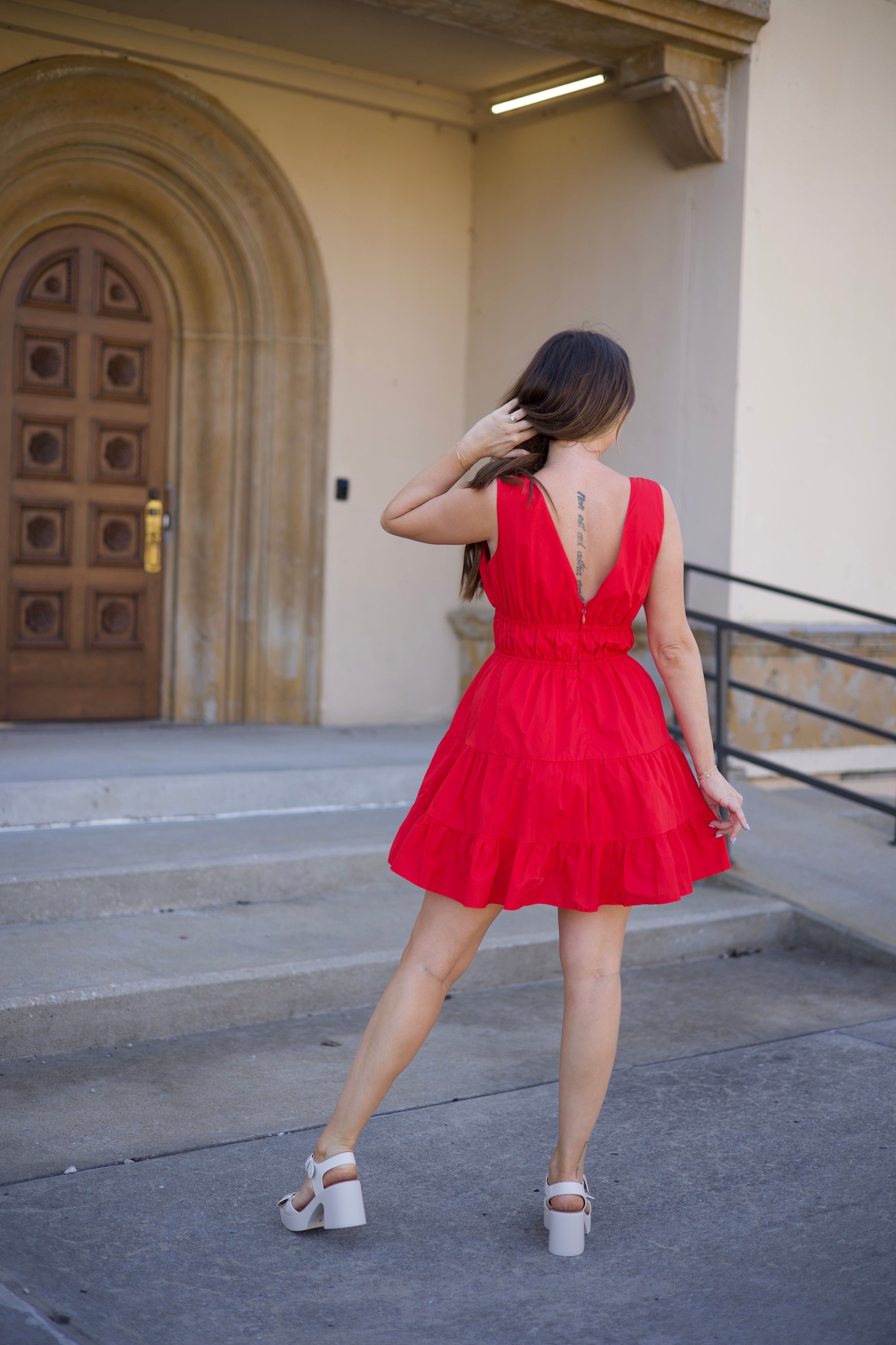 Kerry Tiered Mini Dress in red with a plunging neckline and tiered ruffles, twirling in front of an arched doorway.