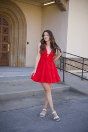 Kerry Tiered Mini Dress in red with a plunging neckline and tiered ruffles, twirling in front of an arched doorway.