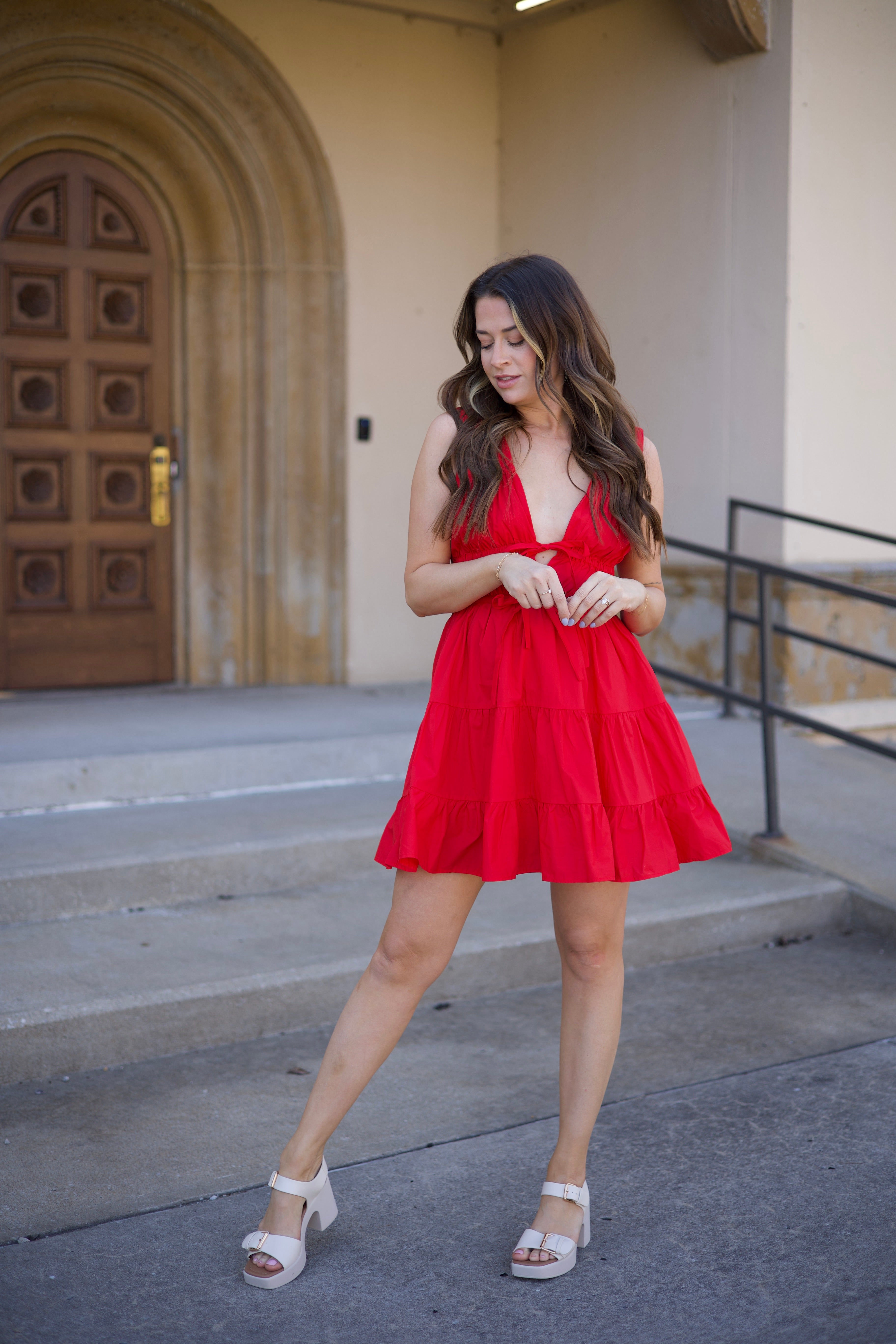 Kerry Tiered Mini Dress in red with a plunging neckline and tiered ruffles, twirling in front of an arched doorway.