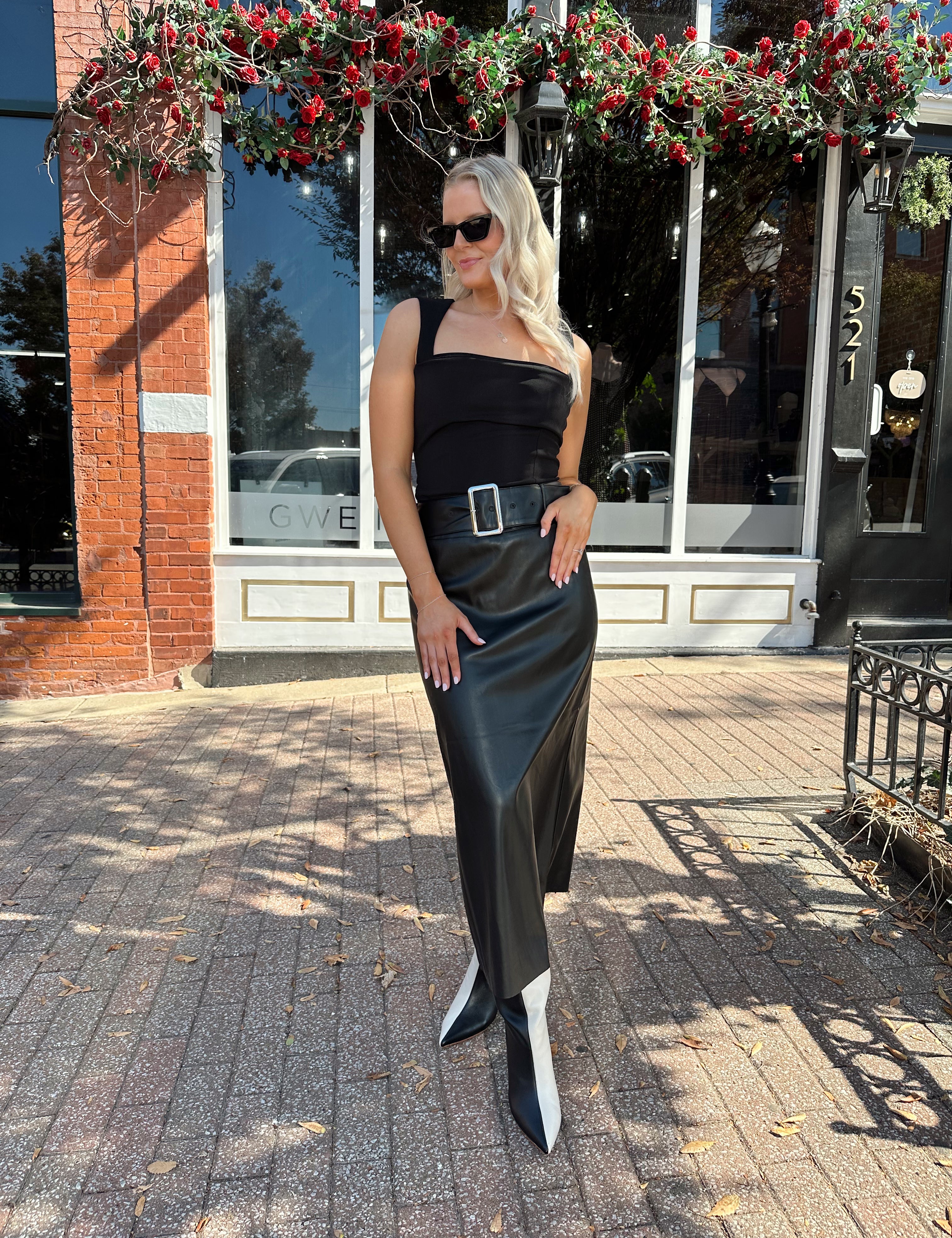 Woman wearing black leather belted midi skirt with black square neck top.