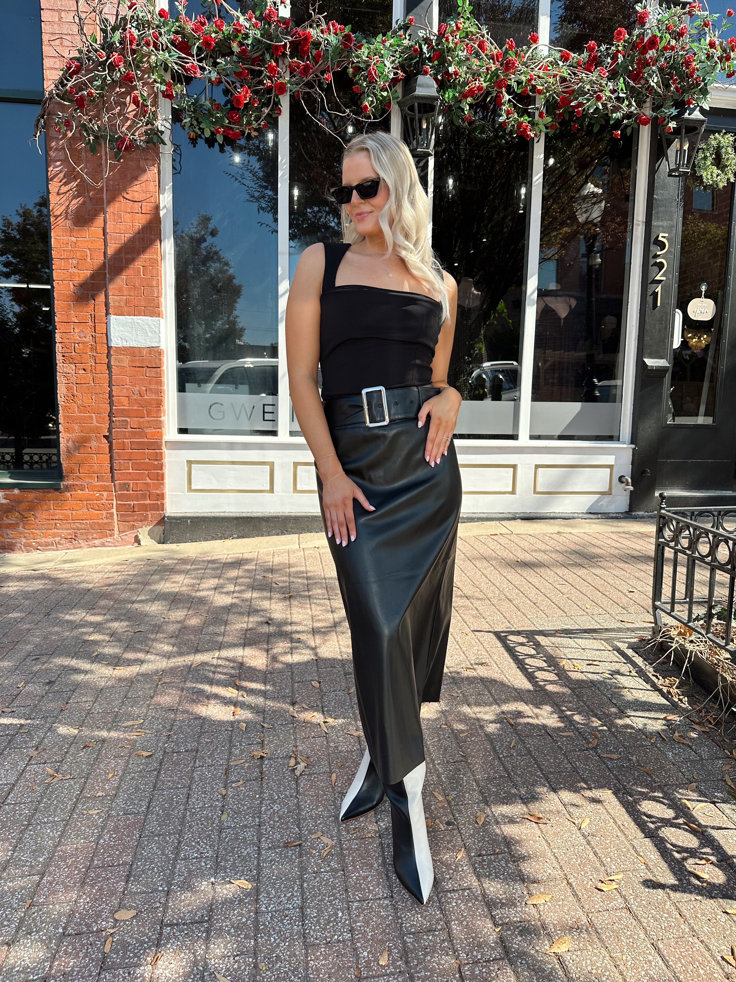 Woman wearing black leather belted midi skirt with black square neck top.