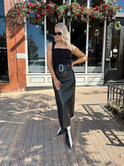 Woman wearing black leather belted midi skirt with black square neck top.