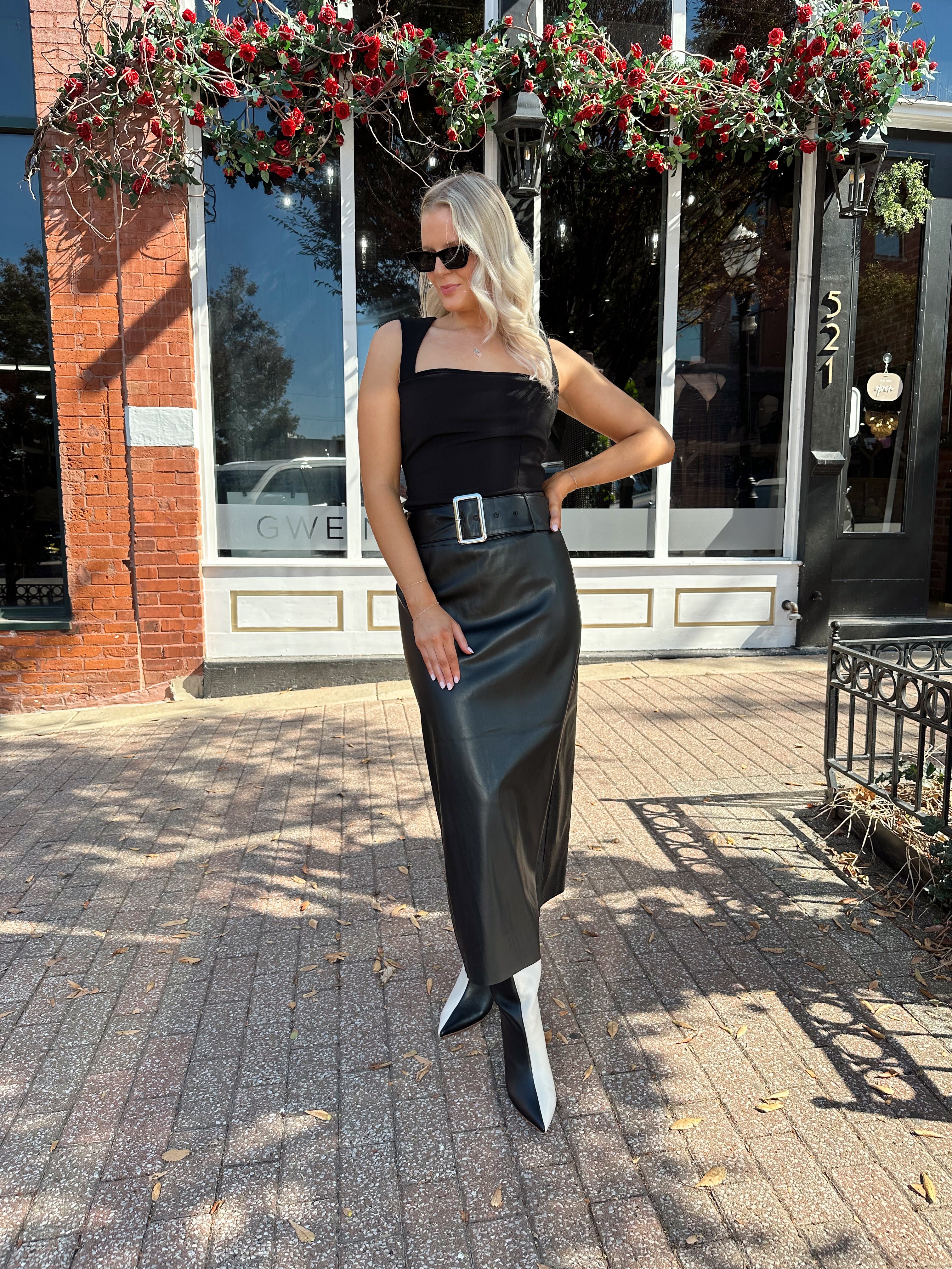 Woman wearing black leather belted midi skirt with black square neck top.