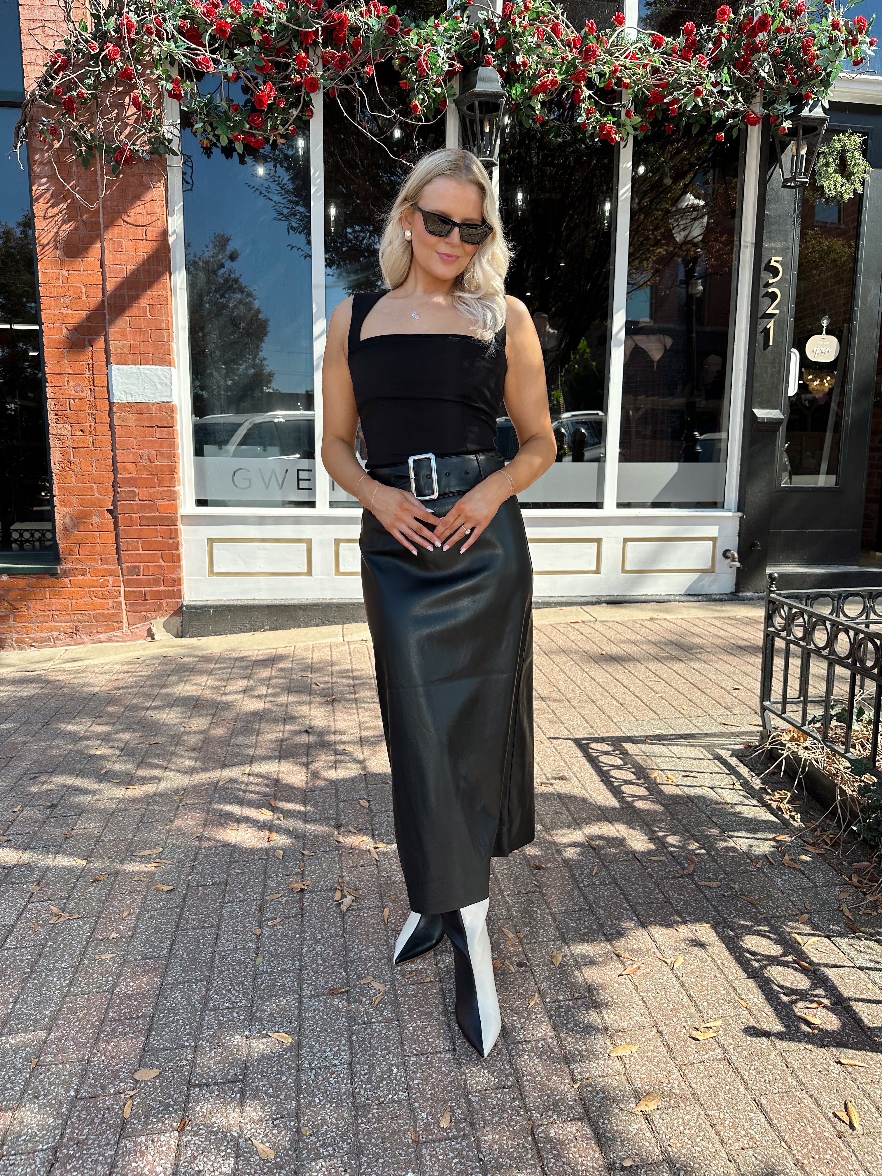 Woman wearing black leather belted midi skirt with black square neck top.