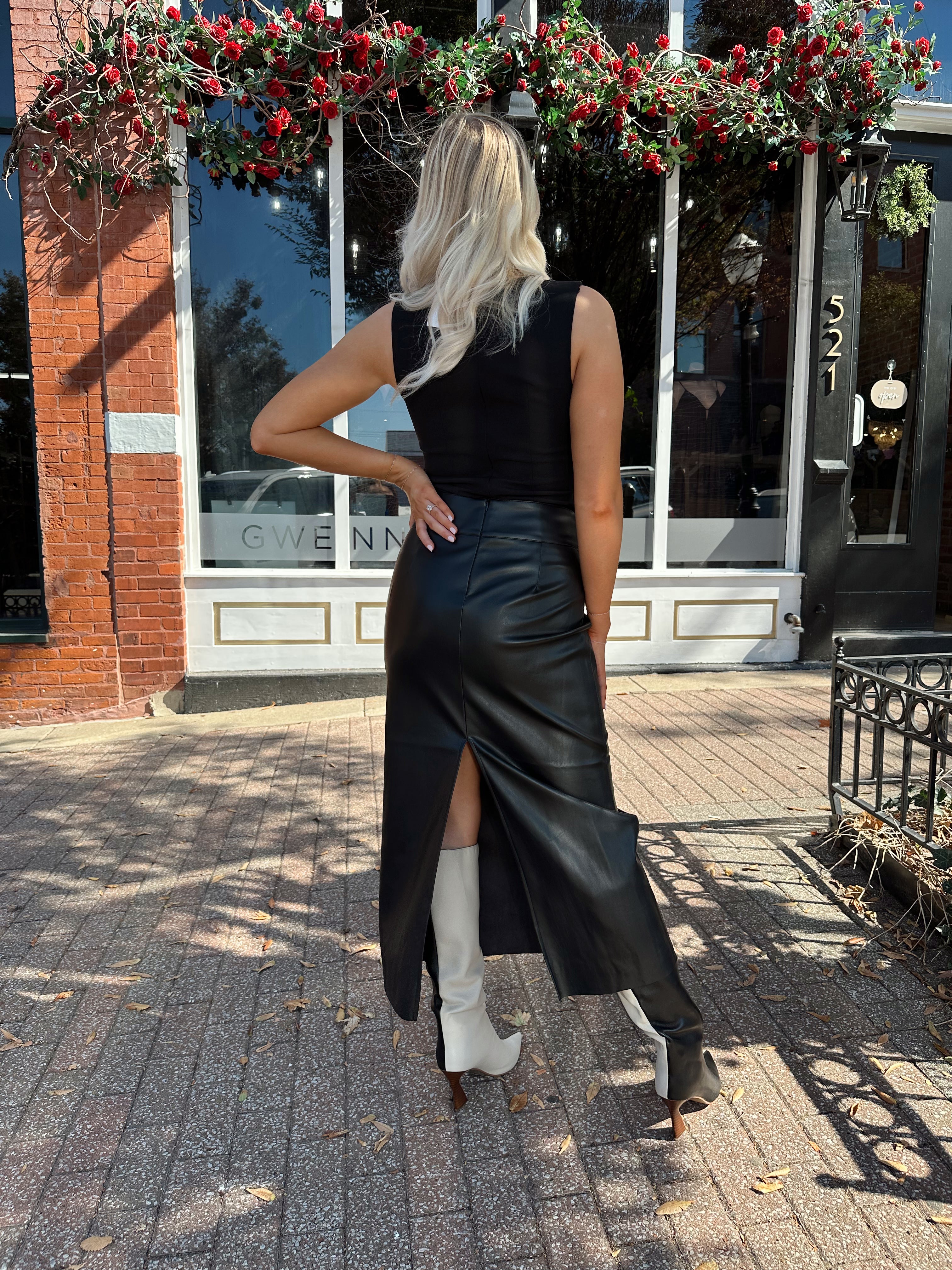 Woman wearing black leather belted midi skirt with black square neck top.