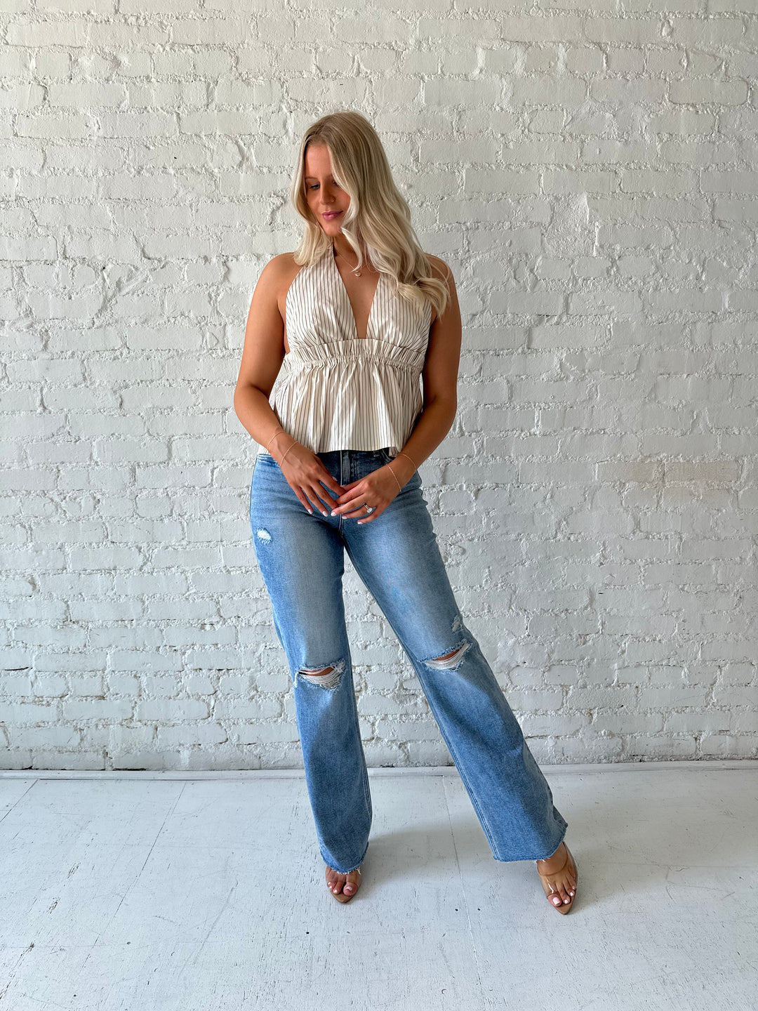 Woman wearing high waisted distressed jeans with striped halter top.