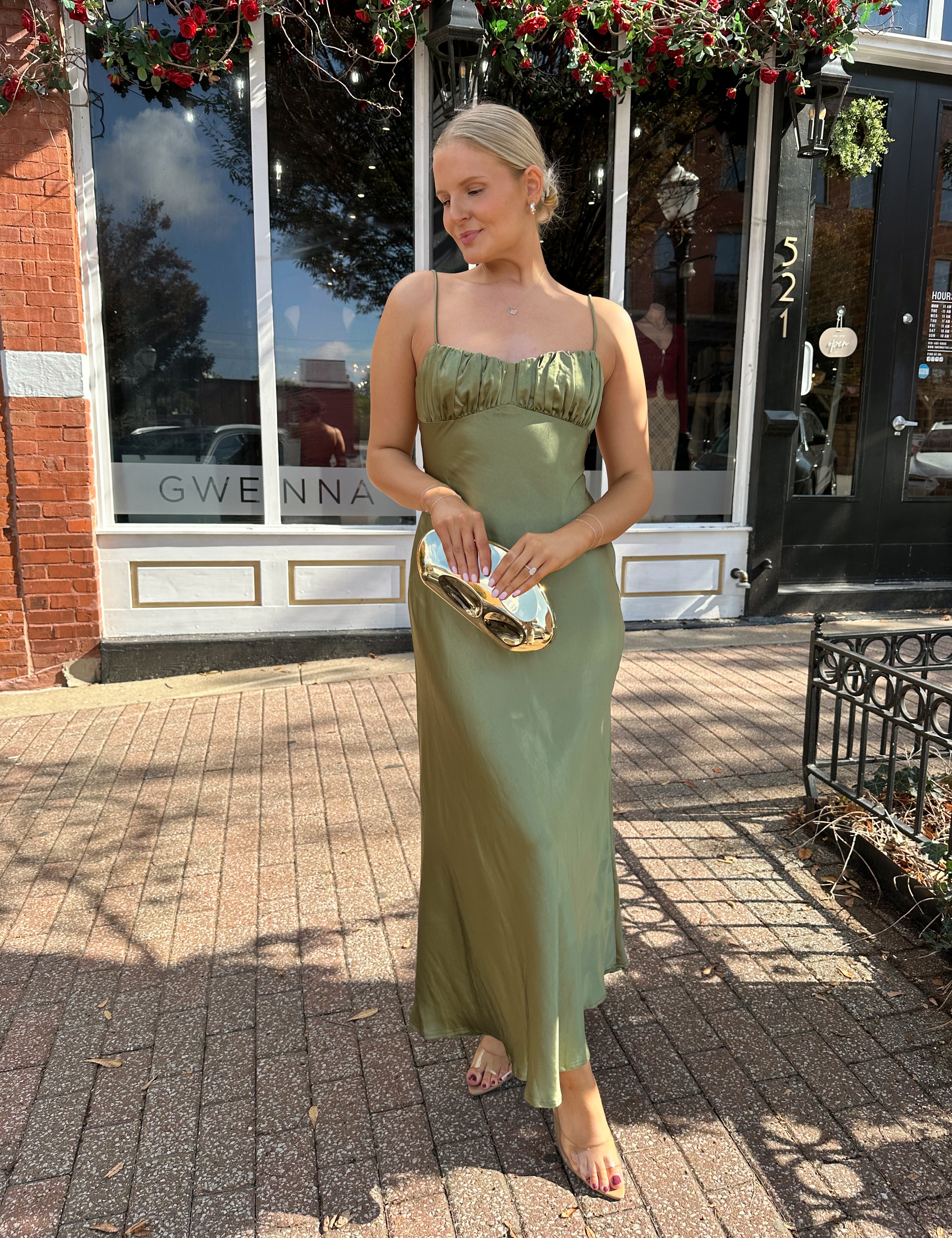 Woman wearing olive green satin maxi dress with open twist back.