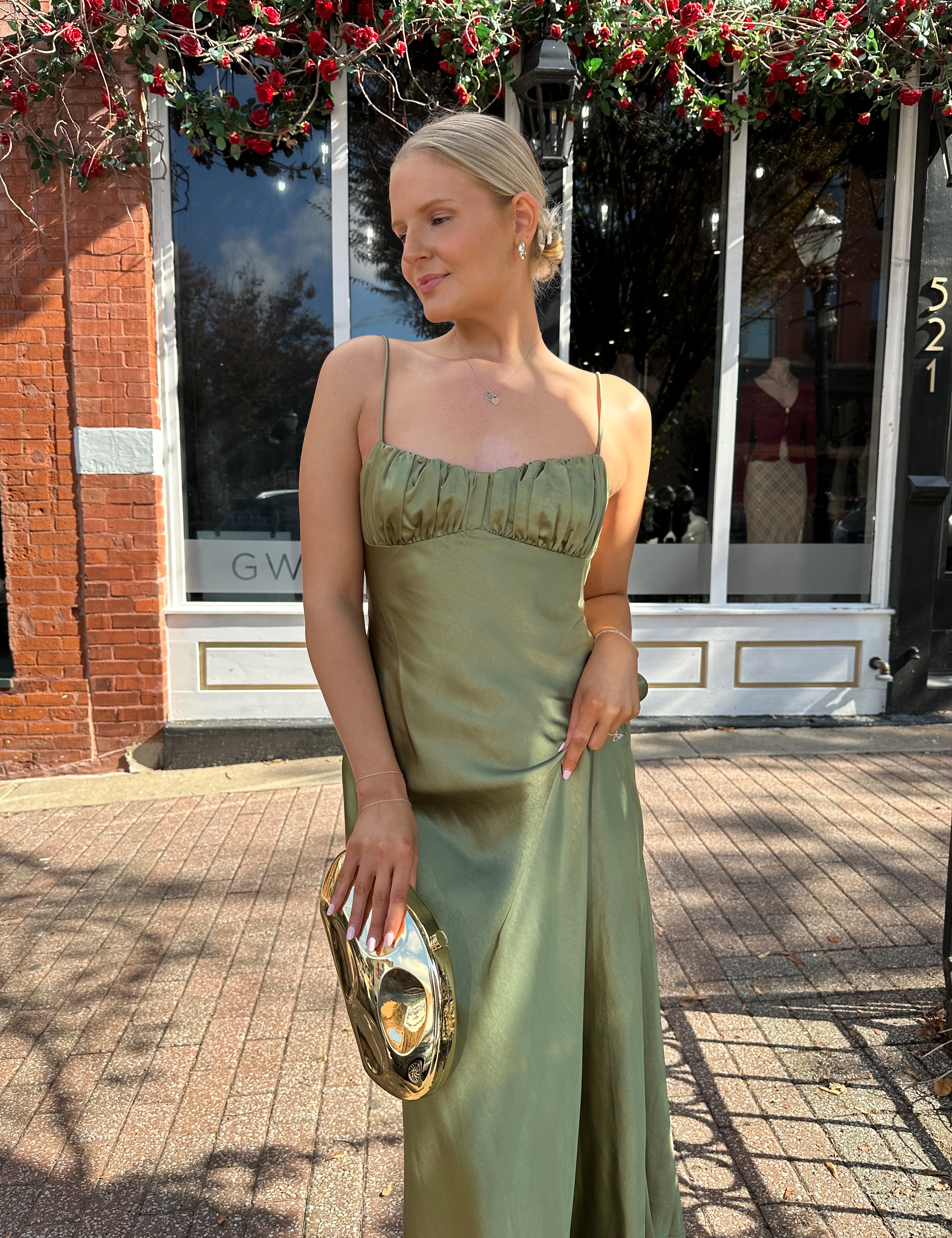 Woman wearing olive green satin maxi dress with open twist back.
