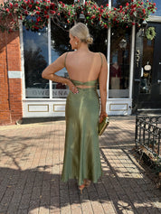 Woman wearing olive green satin maxi dress with open twist back.