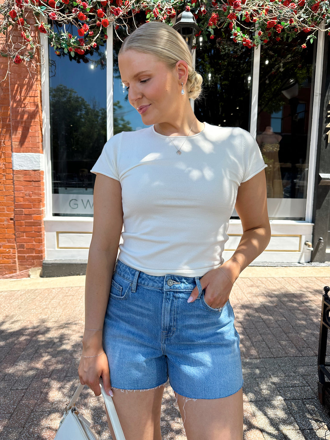 Woman wearing cream colored knit t-shirt and medium wash denim short. 