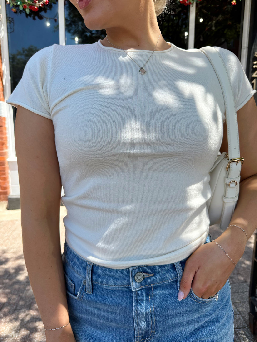 Woman wearing cream colored knit t-shirt and medium wash denim short. 