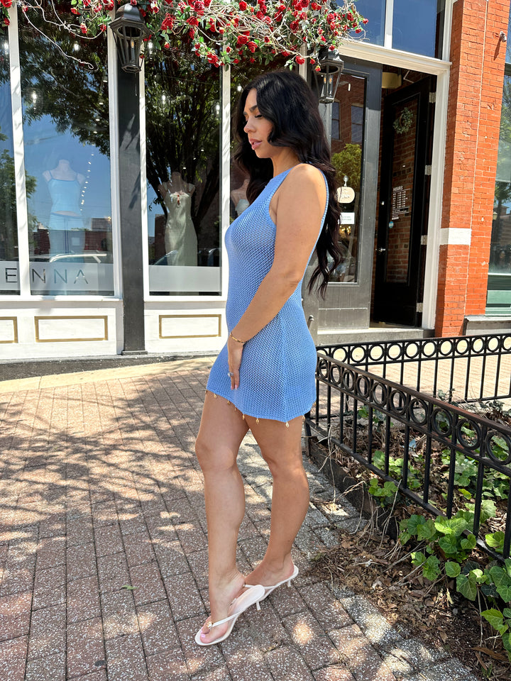 Woman wearing dusty blue knit mini dress with see shell detail on the trim.
