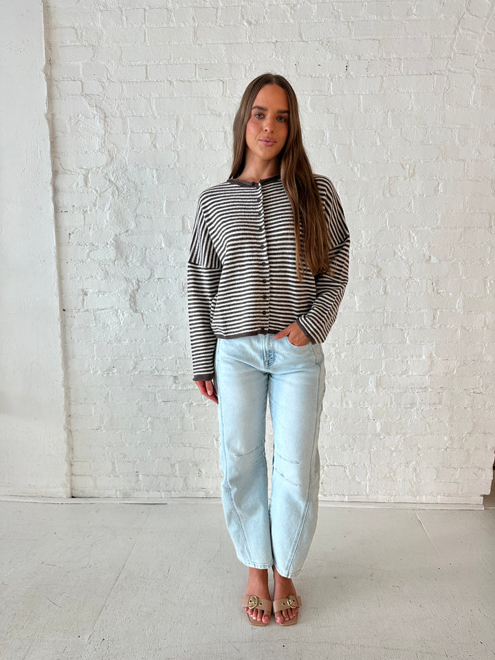 Woman wearing brown and cream striped knit cardigan with light wash barrel jeans. 