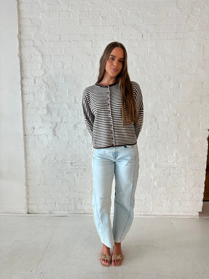 Woman wearing brown and cream striped knit cardigan with light wash barrel jeans. 