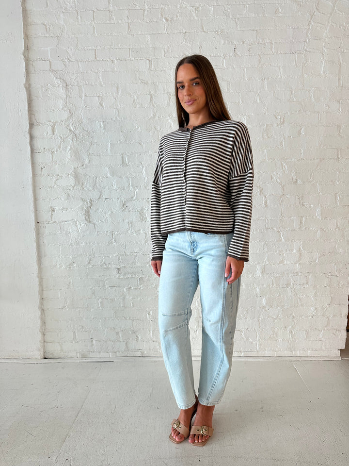 Woman wearing brown and cream striped knit cardigan with light wash barrel jeans. 