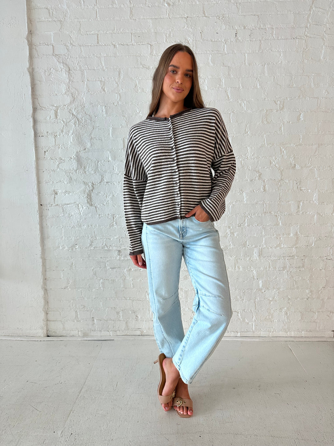 Woman wearing brown and cream striped knit cardigan with light wash barrel jeans. 